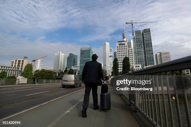 Pedestrian wheels luggage across a bridge towards the skyscrapers of downtown Frankfurt, Germany, on Wednesday, April 25, 2018. About 8,000...