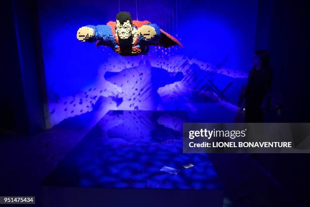 Woman stands next to a super heroe made with Lego bricks by US artist Nathan Sawaya on April 26, 2018 in La Vilette hall in Paris prior the...