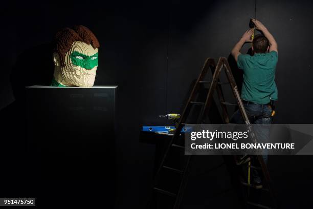 Man works near a head of a super heroe made with Lego bricks by US artist Nathan Sawaya on April 26, 2018 in La Vilette hall in Paris prior the...