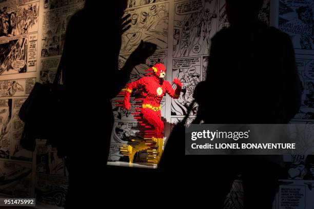 People stand near a sculpture of a super heroe made with Lego bricks by US artist Nathan Sawaya on April 26, 2018 in La Vilette hall in Paris prior...