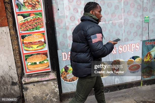 Young man walks past a display of pictures showing fast food outside a shop in Camberwell on April 26, 2018 in London, England. Party leaders have...
