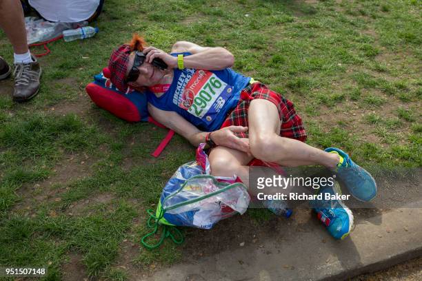 Tired long-distance runner wearing a kilt rests after finishing the London Marathon, in St James's Park, on 22nd April 2018, in London, England.