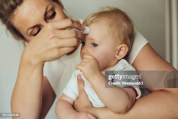 mother using a skin thermometer to take baby’s temperature - body temperature stock pictures, royalty-free photos & images