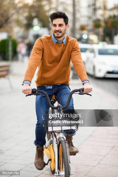 portrait of young man riding rental bike in the city - velofahren stock-fotos und bilder