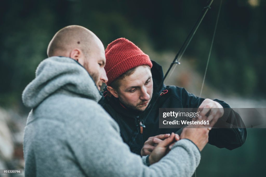 Young man helping friend with fishing rod