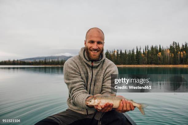 canada, british columbia, portrait of smiling man in canoe holding fish on boya lake - passagier wasserfahrzeug stock-fotos und bilder