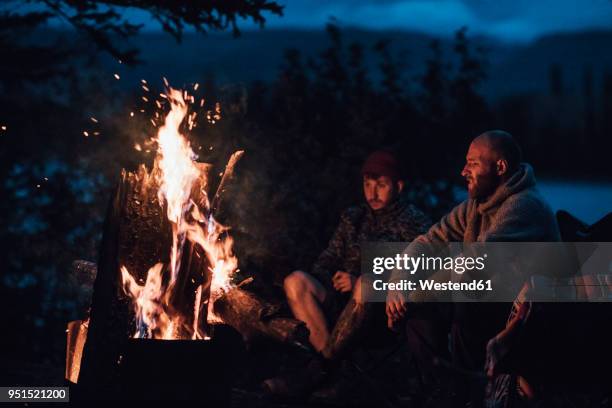 canada, british columbia, two men sitting at camp fire at boya lake at night - campfire fotografías e imágenes de stock
