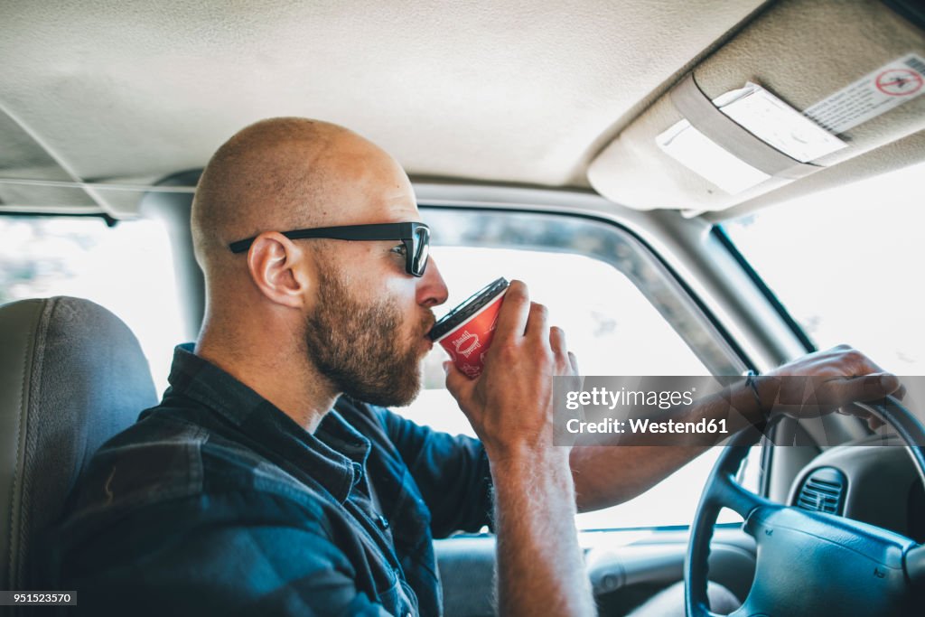 Young man with sunglasses and beard on a road trip with takeaway drink