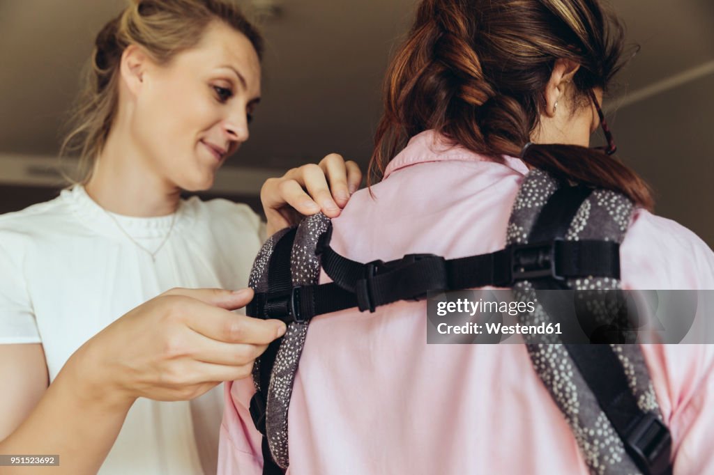 Midwife showing young mother how to fasten a baby sling