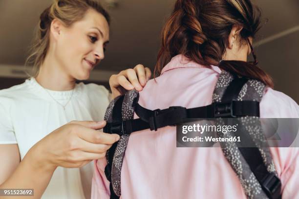 midwife showing young mother how to fasten a baby sling - midwifery stock-fotos und bilder