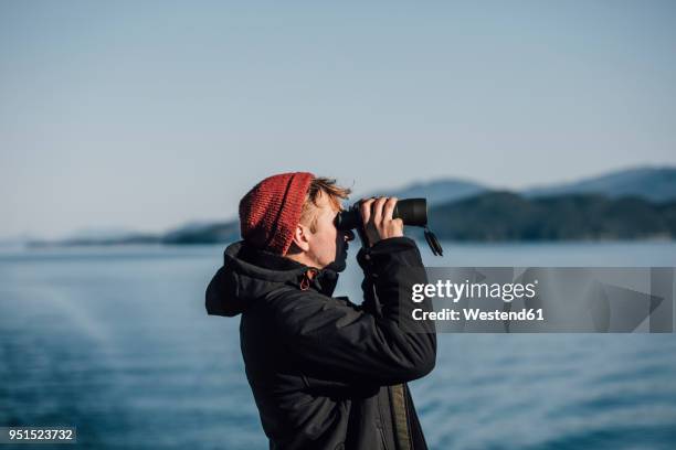 canada, british columbia, man looking through binoculars at the coast - binoculars imagens e fotografias de stock
