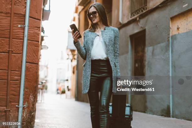 young businesswoman in the city checking cell phone - pantalón fotografías e imágenes de stock