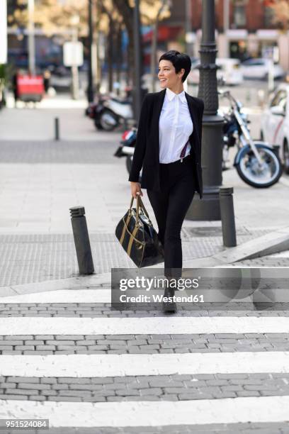 smiling young businesswoman crossing street - black trouser suit stock pictures, royalty-free photos & images