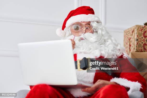 santa claus using laptop with magnifier - miope and humor fotografías e imágenes de stock