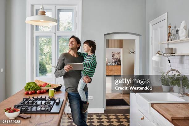 father and son using tablet in kitchen looking at ceiling lamp - family in kitchen stock-fotos und bilder