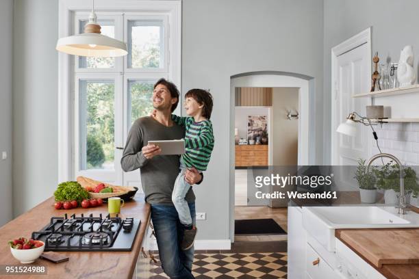 father and son using tablet in kitchen looking at ceiling lamp - remote controlled photos et images de collection