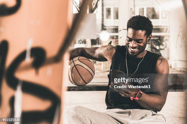 smiling man with tattoos and basketball using smartphone and earphones - basketball all access stock pictures, royalty-free photos & images