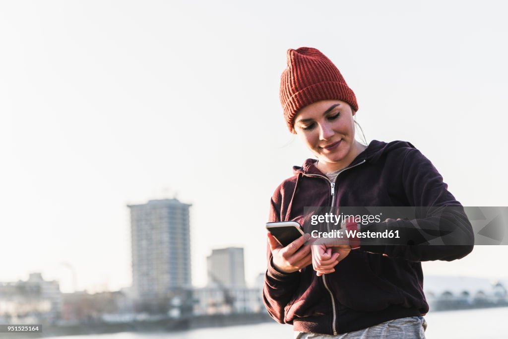 Sportive young woman at the riverside in the city with smartphone and smartwatch