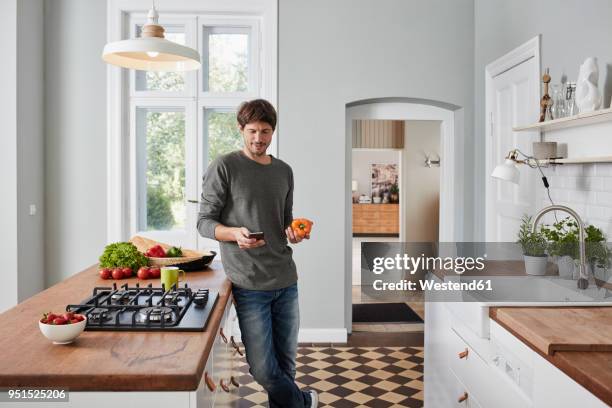 man using smartphone and holding bell pepper in kitchen - homme cuisine photos et images de collection