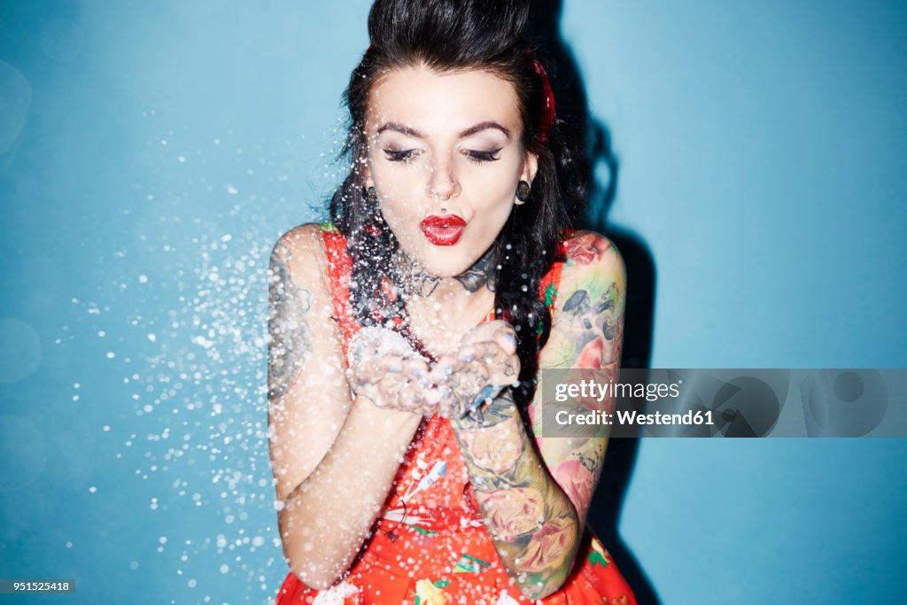 Portrait of tattooed woman blowing artificial snow