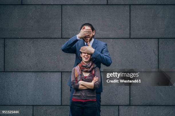 businessman covering laughing woman's eyes - small man and tall woman stock pictures, royalty-free photos & images