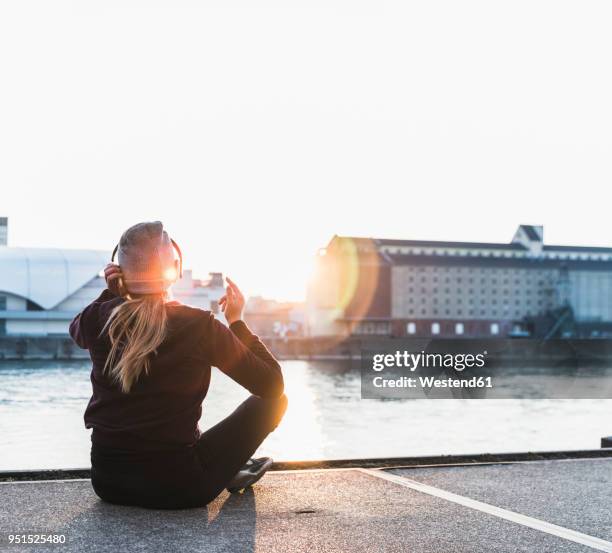 sportive young woman having a break at the riverside in the city at sunset - corredora de footing fotografías e imágenes de stock