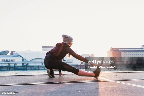 young woman stretching at the riverside in the city at sunset - preparation stock-fotos und bilder