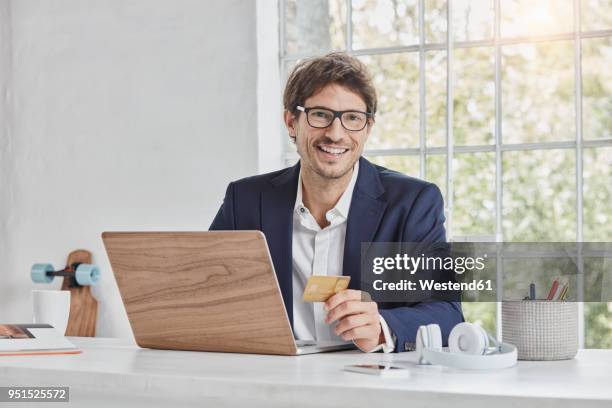 portrait of smiling businessman with laptop on desk holding credit card - skateboard shop stock pictures, royalty-free photos & images