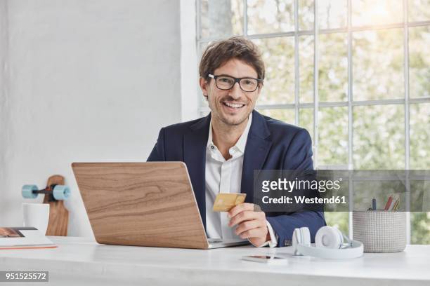 portrait of smiling businessman with laptop on desk holding credit card - business man sitting banking imagens e fotografias de stock