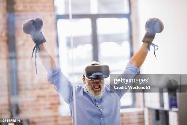 portrait of businessman with virtual reality glasses and boxing gloves in the office - erweiterte realität stock-fotos und bilder