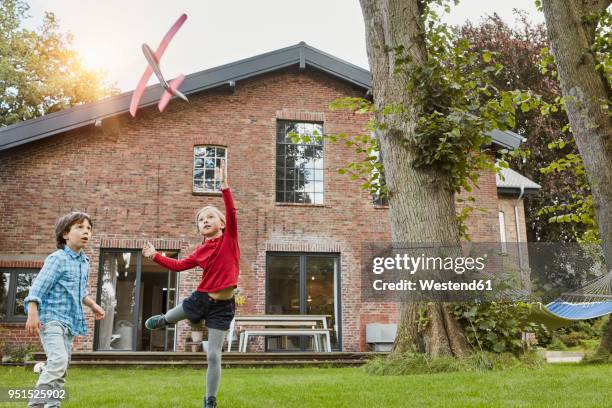 two children playing with toy airplane in garden of their home - hovering fotografías e imágenes de stock