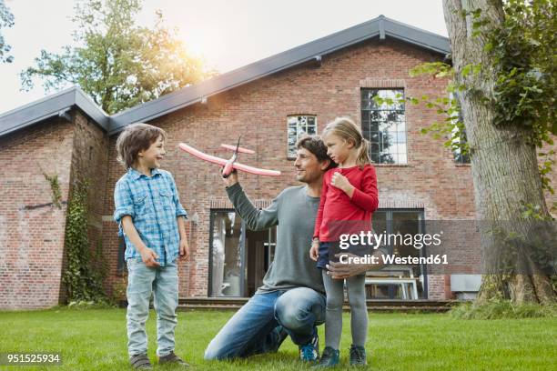 father with two children playing with toy airplane in garden of their home - mittelstand stock-fotos und bilder