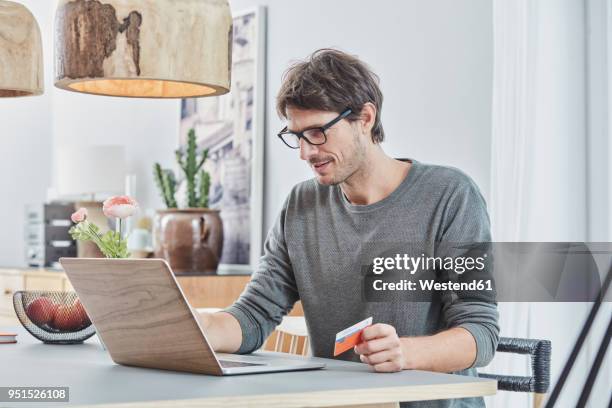 man holding a card using laptop on table at home - mann mit kreditkarte stock-fotos und bilder