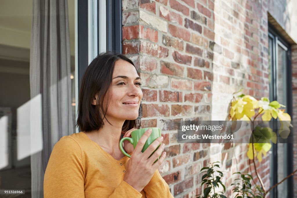 Smiling woman drinking from cup in front of her home