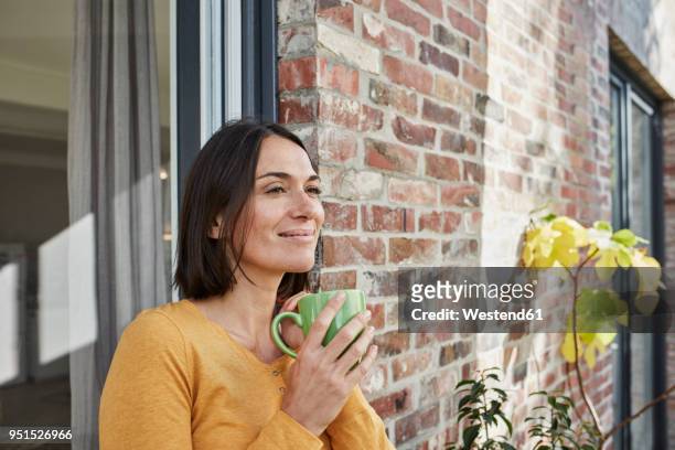 smiling woman drinking from cup in front of her home - mujeres de mediana edad fotografías e imágenes de stock