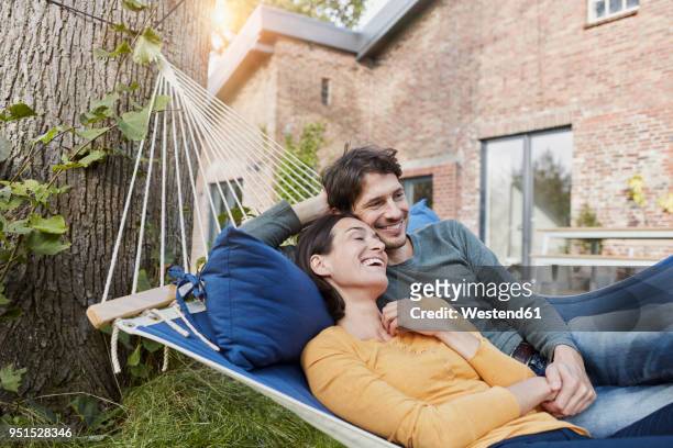 happy couple lying in hammock in garden of their home - mid adult stock-fotos und bilder