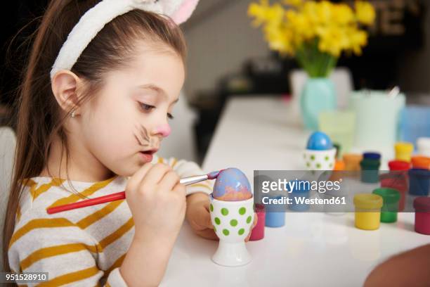girl with bunny ears sitting at table painting easter eggs - bunny eggs stock-fotos und bilder