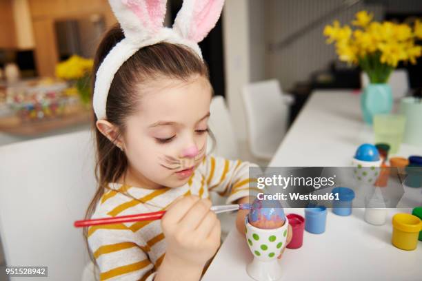 girl with bunny ears sitting at table painting easter eggs - easter bunny ears stock pictures, royalty-free photos & images