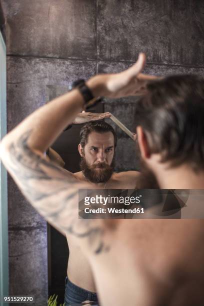 portrait of bearded man looking at his mirror image while combing his hair - man combing hair stock pictures, royalty-free photos & images