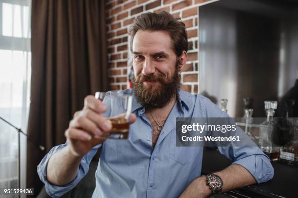 portrait of smiling man with glass of whiskey at home - status symbol stock pictures, royalty-free photos & images