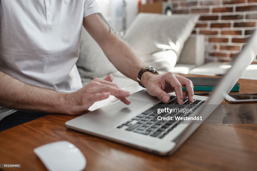 Man's hands on keyboard and touchpad of laptop, partial view