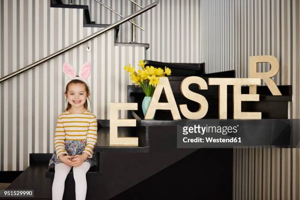 portrait of smiling girl with bunny ears sitting on stairs next to word 'easter' - easter bunny ears ストックフォトと画像