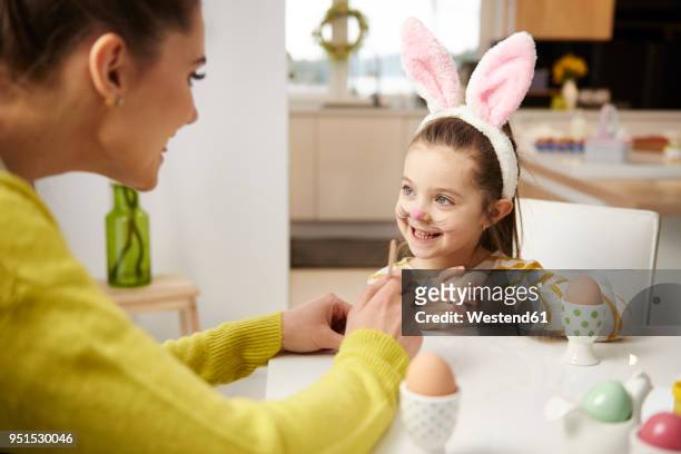 girl with bunny ears and mother sitting at table with easter eggs - easter bunny ears ストックフォトと画像
