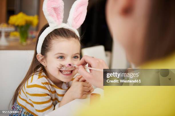 mother painting daughter's face wearing bunny ears - face painting imagens e fotografias de stock