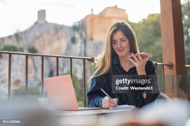 spain, alquezar, portrait of smiling young freelancer with laptop and cell phone working on terrace - travel writer stock pictures, royalty-free photos & images