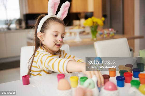 girl with bunny ears sitting at table painting easter eggs - easter bunny ears ストックフォトと画像