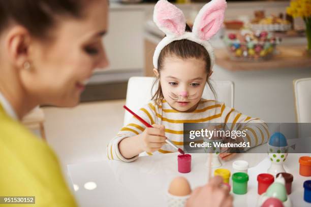 mother and daughter with bunny ears sitting at table painting easter eggs - easter bunny ears ストックフォトと画像