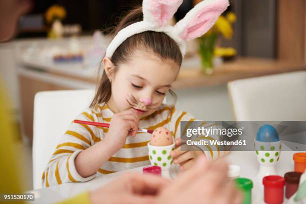 girl with bunny ears sitting at table painting easter eggs - easter bunny ears ストックフォトと画像