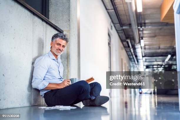 portrait of smiling mature businessman sitting on the floor - einzelner mann über 40 stock-fotos und bilder