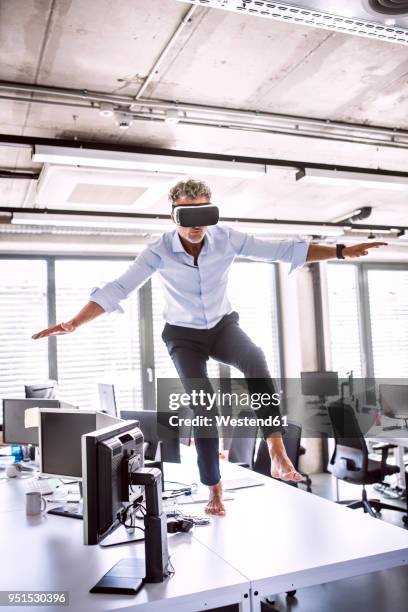 barefoot mature businessman on desk in office wearing vr glasses - new adventure stock pictures, royalty-free photos & images